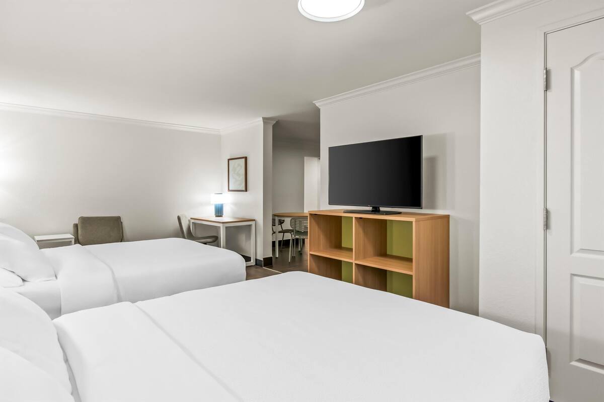 Et hotelværelse med to senge, et skrivebord med stol, et fjernsyn og et klædeskab.
