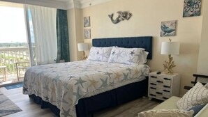 Un dormitorio con cama, mesitas de noche, sofá y balcón con cortinas.