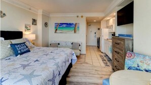 Un dormitorio con una cama, un aparador, un televisor y un cuadro de una playa.