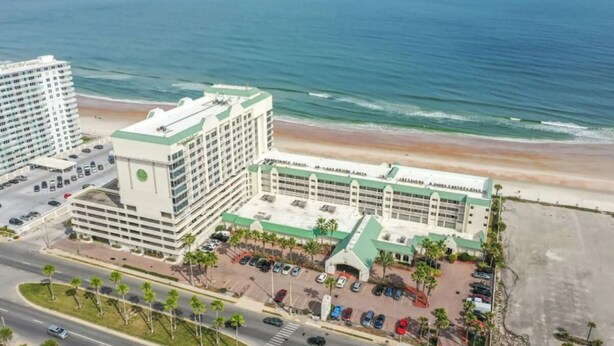 Un hotel con estacionamiento, vista al mar y una carretera en primer plano.