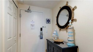 Un pasillo con una puerta blanca, un espejo con marco decorativo y una pequeña mesa con adornos náuticos.