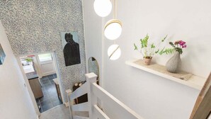 A staircase with a patterned wall, a black portrait, and a shelf with plants and a vase.