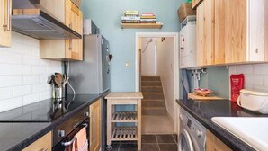A compact kitchen with wooden cabinets, a black countertop, a built-in oven, a washing machine, and a small wooden cart.