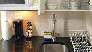 Une cuisine équipée d’un four à micro-ondes, d’une machine à café et d’un évier. Des étagères se trouvent au-dessus de l’évier, où sont rangées la vaisselle et les tasses.