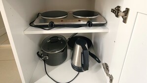Une cuisine avec un meuble blanc contenant une cuisinière, deux poêles, une bouilloire et une casserole.