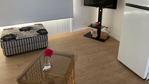 A modern living room with a sofa, a glass coffee table with a vase, a flat-screen TV, and a refrigerator. - Seacret, only 300 m to the beach! (St Leonards)