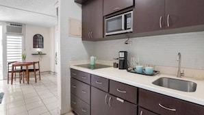 A modern kitchen with dark wooden cabinets, a microwave, a coffee maker, and a sink. - Studio 3 minutes to the airport| Free Parking|Pool (Carolina)