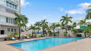 A rectangular swimming pool with a clear blue water, surrounded by a concrete deck. There are lounge chairs and palm trees around the pool. - Studio 3 minutes to the airport| Free Parking|Pool (Carolina)