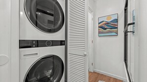 A laundry room with two front-loading washing machines, a control panel, and a door leading to another room.