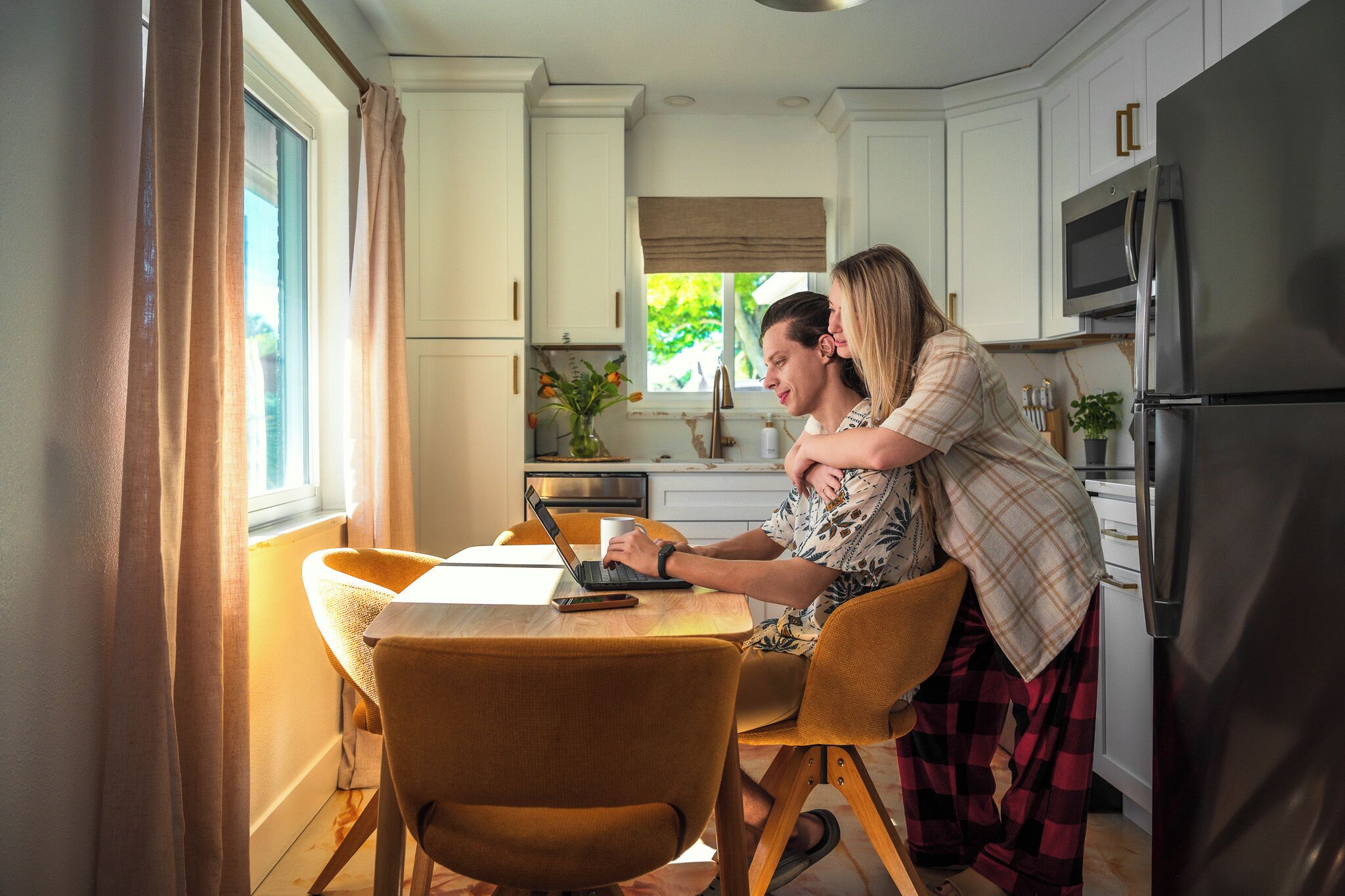 A modern kitchen with white cabinets, a stainless steel refrigerator, and a dining area with a wooden table and chairs.