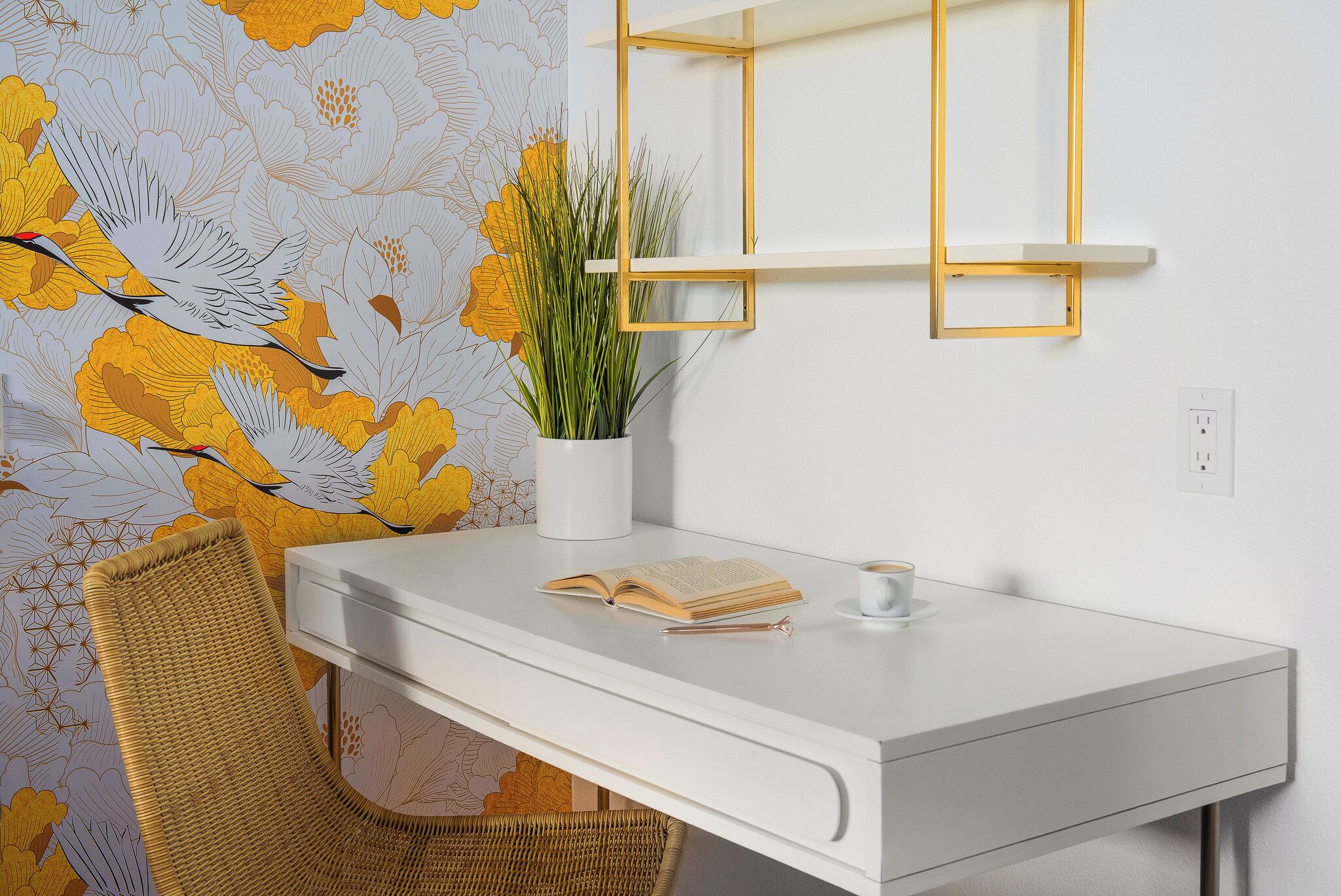 A white desk with a book and a pen, a potted plant, and a chair.