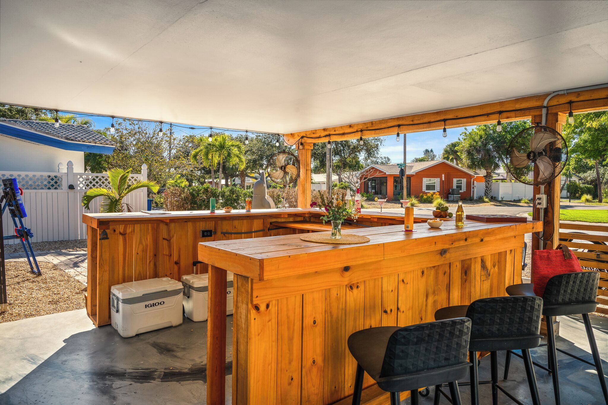 A wooden outdoor bar area with a covered roof, a seating arrangement, and a view of a residential neighborhood.
