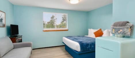 Quarto com cama, sofá, televisão e pequena cozinha.