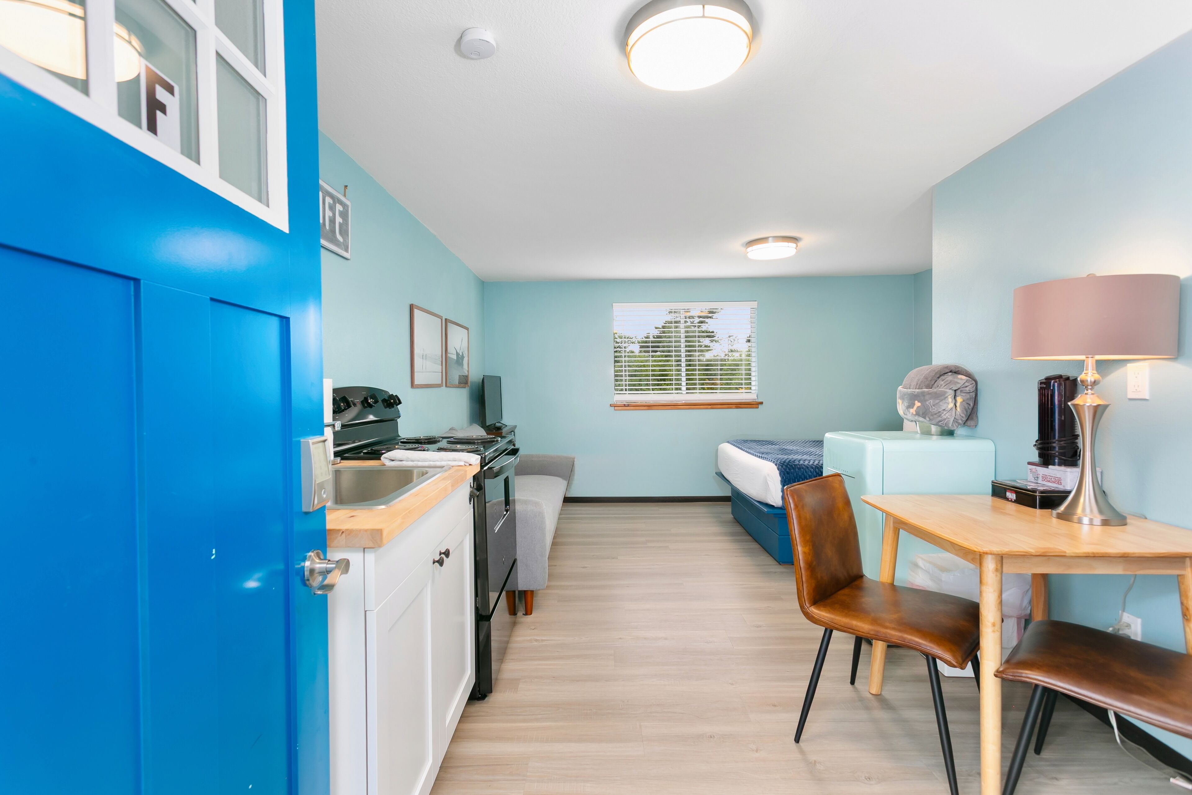 A compact room with a kitchenette, a bed, a desk, and a chair.