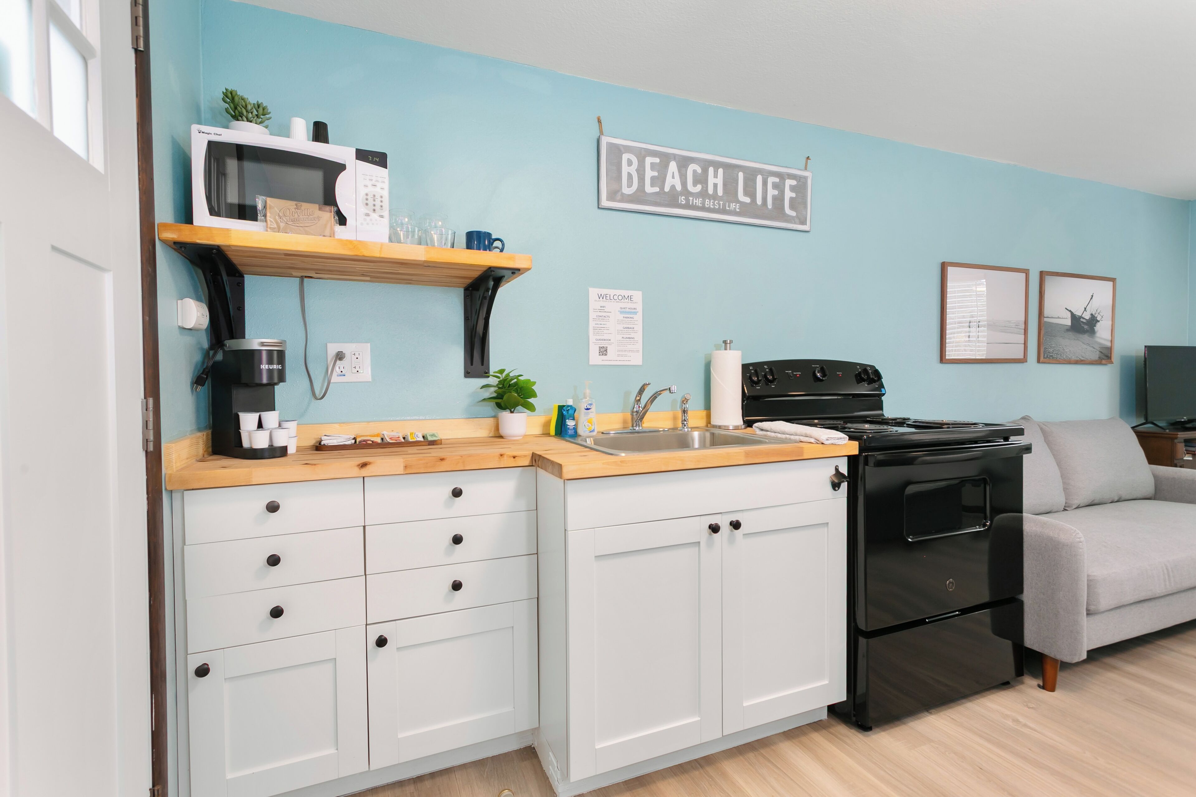 A kitchen with white cabinets, a black stove, a wooden countertop, and a blue wall.