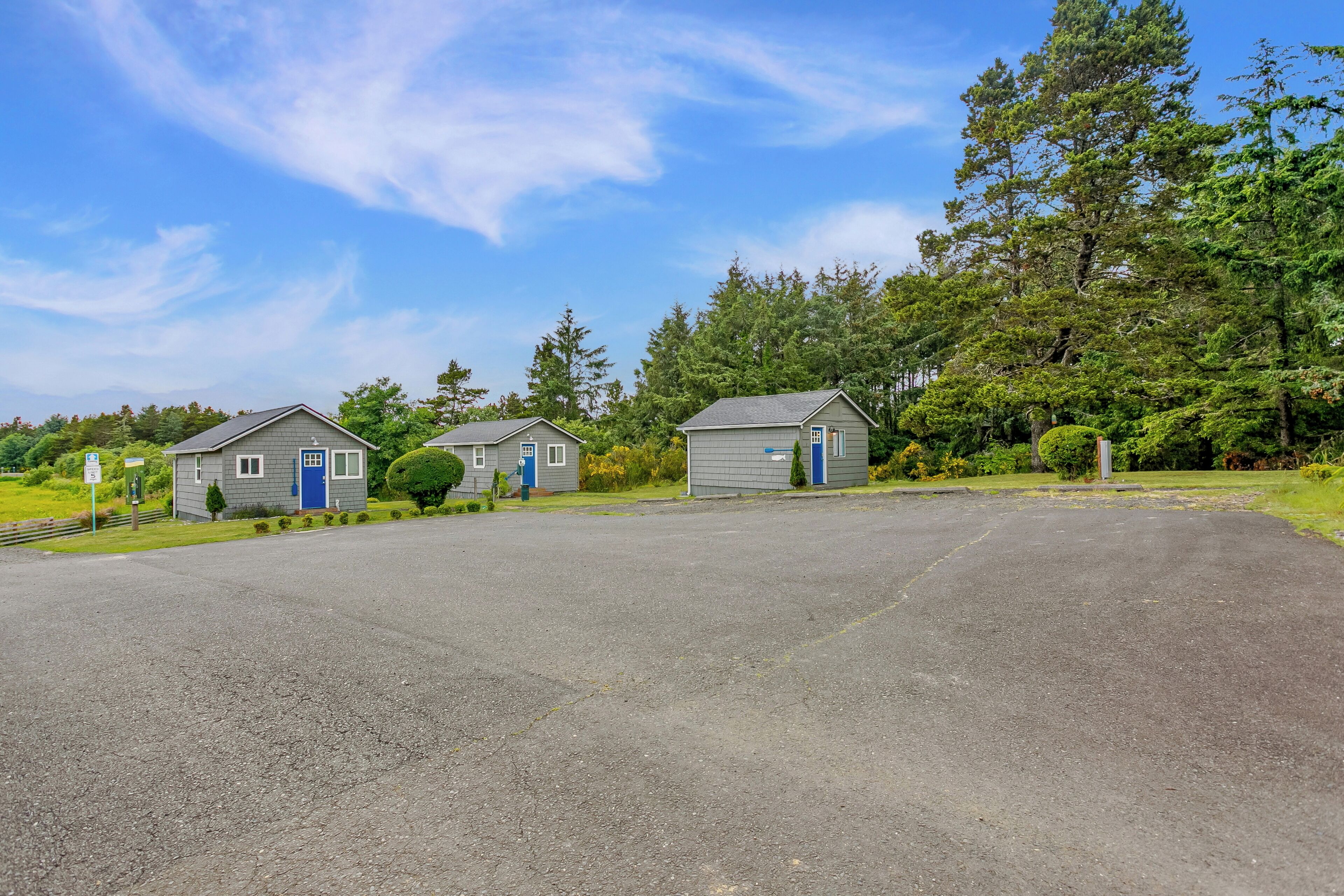 A parking lot with two small buildings, each with a blue door and a small porch area.