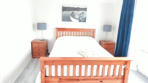 Een slaapkamer met een houten bed, twee nachtkastjes, een lamp, een schilderij en een blauw gordijn.