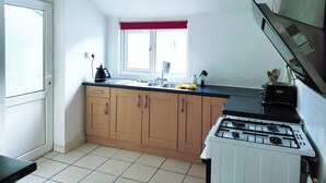 Een keuken met een gasfornuis, houten kastjes, een raam met rode gordijnen en een spoelbak.