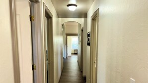 Un pasillo con suelo de madera, paredes blancas y puertas que dan a varias habitaciones.