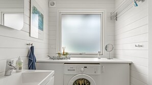 Une petite buanderie moderne et fonctionnelle, dotée d’un lave-linge et d’un sèche-linge intégrés, d’une fenêtre et d’un petit miroir fixé au-dessus du plan de travail.