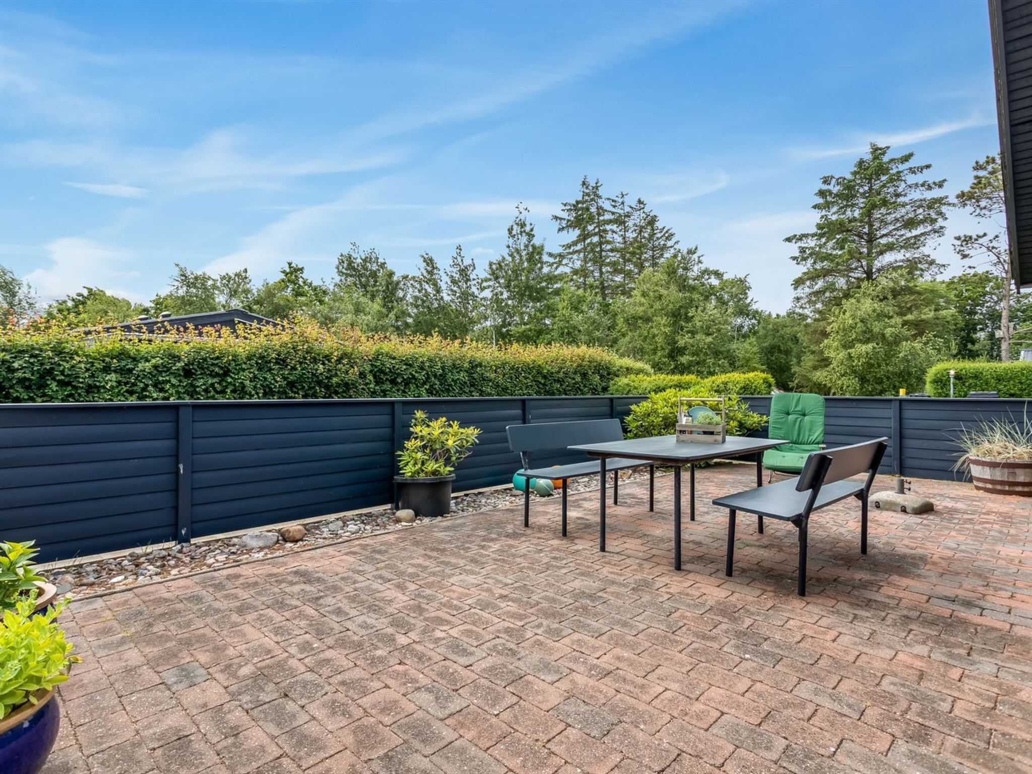 A patio with a brick floor, a black fence, and outdoor furniture including a table and chairs.