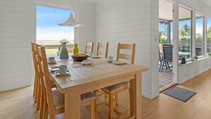 Un coin repas avec une table et des chaises en bois, un luminaire suspendu et une vue sur l’extérieur.