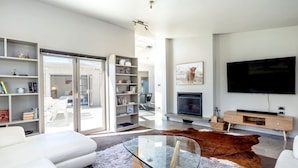 A modern living room with a glass coffee table, white sofas, a leather rug, and a mounted TV.