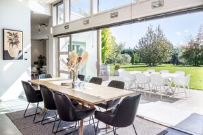 A modern dining area with a wooden table, black chairs, and a view of a garden through large glass doors. - Paradise on Campbell (Martinborough)