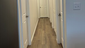 A hallway with wooden flooring, white doors, and recessed ceiling lights.