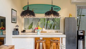 A kitchen with a central island, two hanging light fixtures, a refrigerator, and a surfboard decoration on the wall. - Villa Pia Pererenan (Munggu)