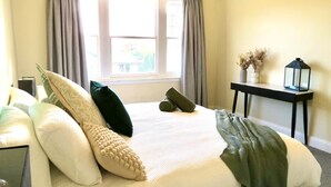 A neatly made bed with pillows and a blanket, a bedside table with a lamp, and a window with curtains. - 11Eardley|5min to CBD | 2 Bedrooms | Free parking (South Launceston)