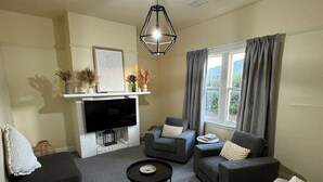 A living room with a fireplace, a flat-screen TV, grey sofas, and a ceiling fan. - 11Eardley|5min to CBD | 2 Bedrooms | Free parking (South Launceston)
