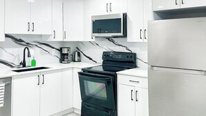 Een moderne keuken met witte kasten, een zwarte kookplaat, een roestvrijstalen koelkast en een magnetron boven de kookplaat.