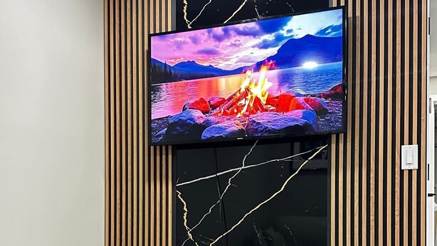 Een moderne woonkamer met een flatscreen televisie bevestigd aan een zwarte marmeren muur, twee ronde tafels en verticale houten latten.