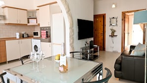 A modern kitchen with a dining area, a flat-screen TV, and a living room with a sofa.