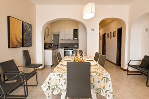 A dining area with a table set for six, surrounded by chairs, with a kitchen in the background.