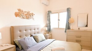 A bedroom with a tufted headboard, a bed with pillows, a bedside table with a lamp, a dresser, and a window with curtains. - Sea & Valley Views Żebbuġ Gozo, Żebbuġ Gozo, Malta (Żebbuġ Gozo)