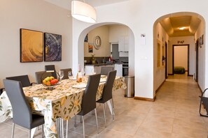 A dining area with a table set for four, chairs, a fruit bowl, and a bottle of wine. - Sea & Valley Views Żebbuġ Gozo, Żebbuġ Gozo, Malta (Żebbuġ Gozo)