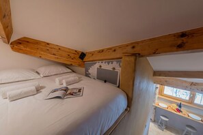 A bedroom with a bed, pillows, towels, a magazine, a window, and a small kitchenette area.