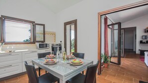 A modern kitchen with white cabinets, a microwave, and a dining area with a glass table and chairs.