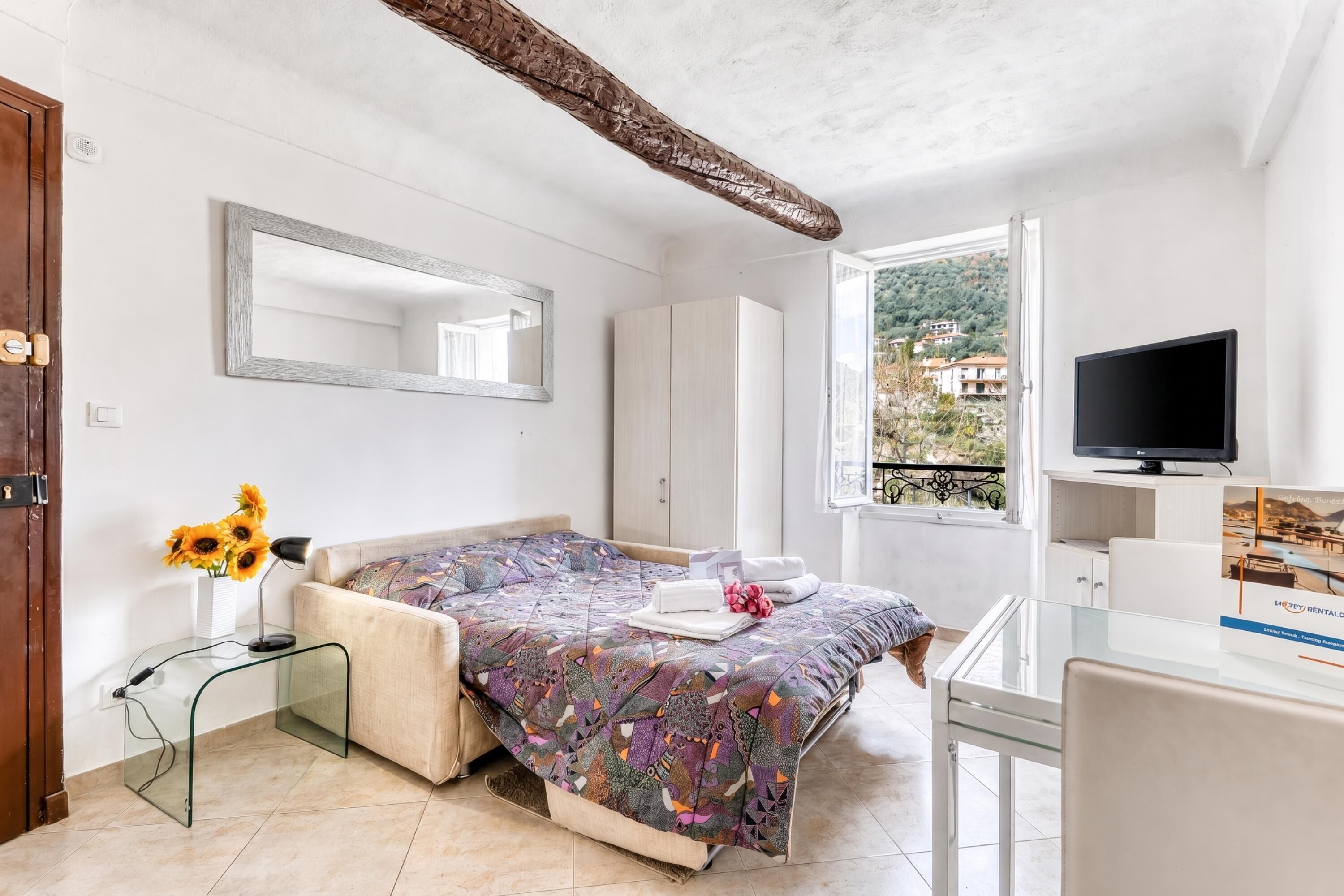 A bedroom with a bed, a TV, a window with a view, and a mirror.