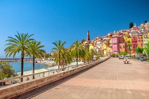 A seaside promenade with palm trees, colorful buildings, and a clear blue sky.