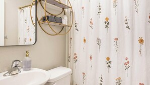 Ett badrum med ett vitt handfat, en toalett och ett duschdraperi med blommönster.