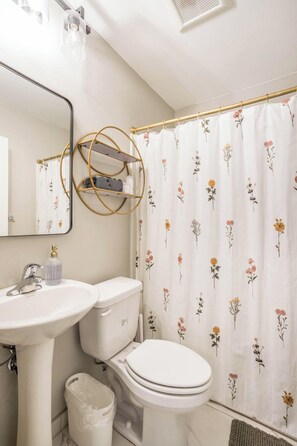 Un bagno con lavandino, water e tenda da doccia a motivi floreali.