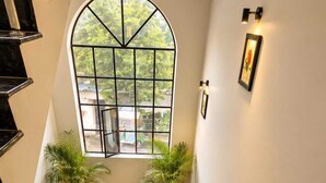 Un escalier muni d’une rampe, des plantes en pot et une grande fenêtre en arc de cercle offrant une vue sur la verdure.