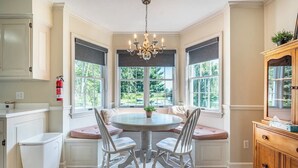 A kitchen with a round table, white chairs, a chandelier, and a view of greenery outside. - Amish Country Getaway w/ Hot Tub & Views (Applecreek)
