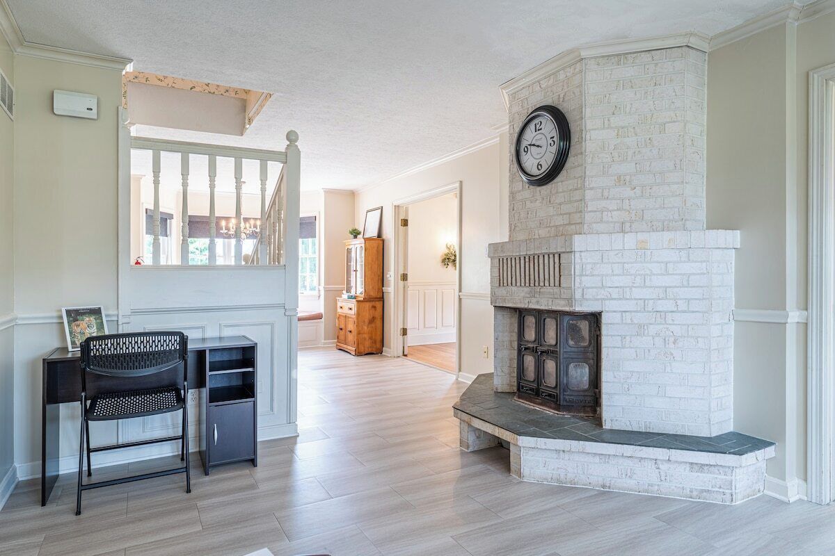 A living room with a fireplace, a clock, and a staircase leading to another room.