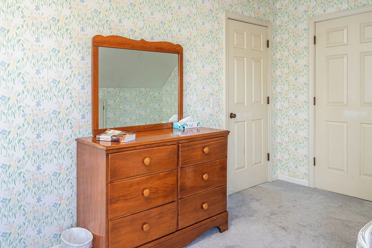 Une commode en bois avec un miroir, une porte et un papier peint à motifs floraux.