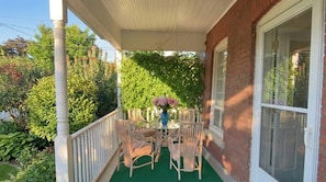 Une véranda abritée, avec une table et des chaises, entourée de verdure.