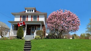 A two-story house with a front porch, a Canadian flag, and a large flowering tree. - Private Room Honey Room 15 MINS WALK to Falls (Niagara Falls)
